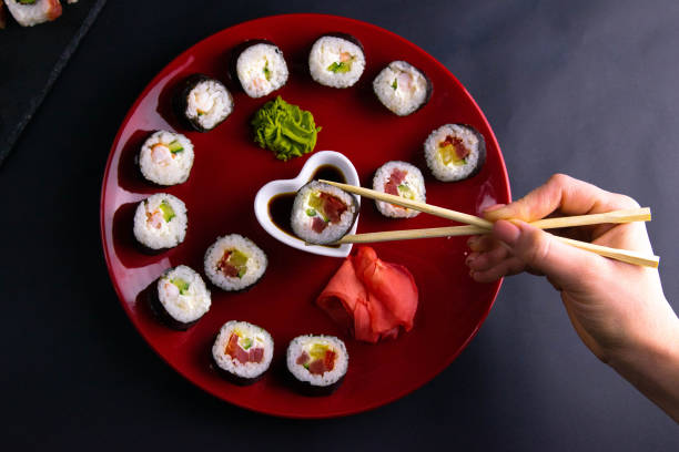 istock Sushi stick keeps roll over soy sauce. Rolls of different kinds are laid out on a red plate along with soy sauce, wasabi and sushi sticks 1205400069