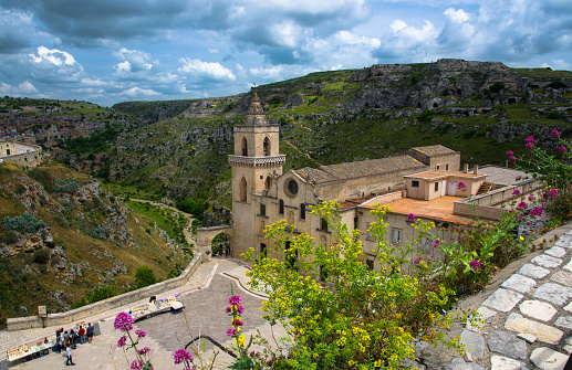 Church Chiesa San Pietro Caveoso, canyon and and ravine with caves di Murgia Timone in historical centre old ancient town Sassi di Matera with blue sky white clouds, UNESCO, Basilicata, Southern Italy