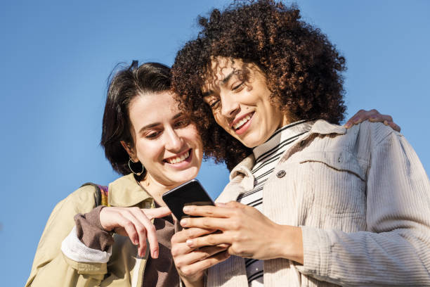istock two young women smiling while looking at phone 1205401293