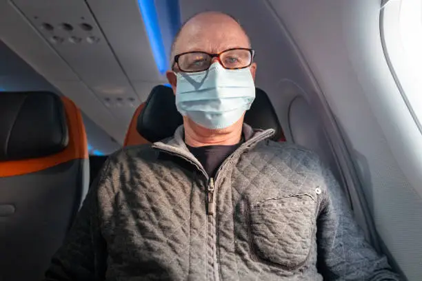 Senior man sitting on a commercial jetliner, wearing protective mask against transmissible infectious diseases and as protection against pollution and the flu.