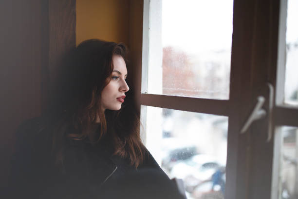 istock Side view of thoughtful woman looking through window 1205408665