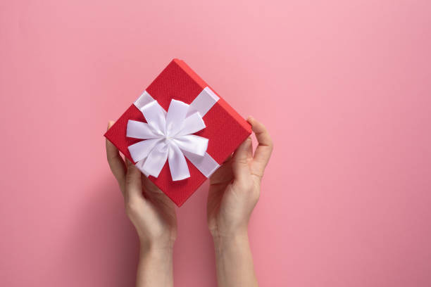 istock Valentine's Day celebration concept. A nice gift from a loved one. Box with a bow in female hands on a delicate pink background. Copy space. Flat lay. 1205423107