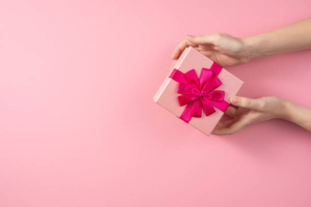 istock Valentine's Day celebration concept. A nice gift from a loved one. Box with a bow in female hands on a delicate pink background. Copy space. Flat lay. 1205423117