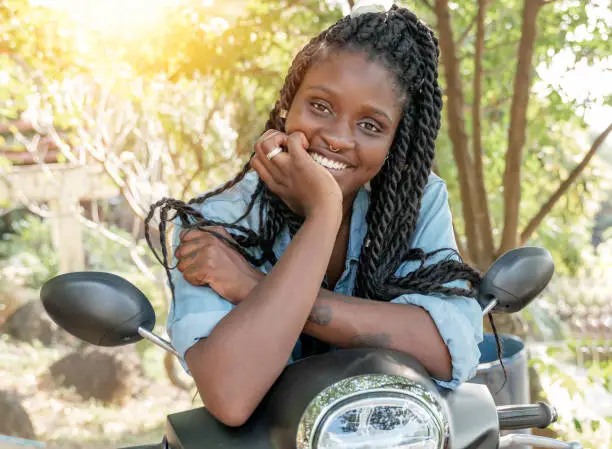 Charming young african american girl woman with a perfect smile and black pigtails with piercings on her face sitting on a motobike