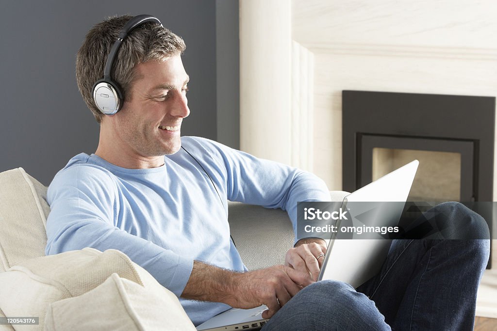 Man Using Laptop Wearing Headphones Relaxing Sitting On Sofa  30-39 Years Stock Photo