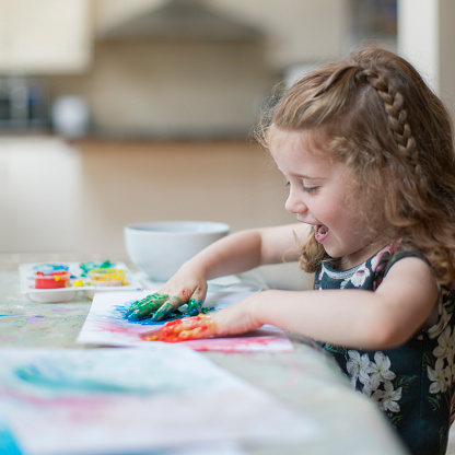 A happy little girl is finger painting at home.