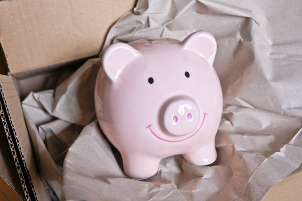 istock Piggy bank inside an open brown cardboard box. 1205443316