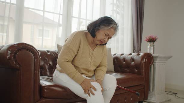 senior woman sitting on couch and massage her knee Portrait elderly woman sitting on couch and suffering from pain her knee, she try to massage, senior healthy concept standing had to knee pose stock pictures, royalty-free photos & images