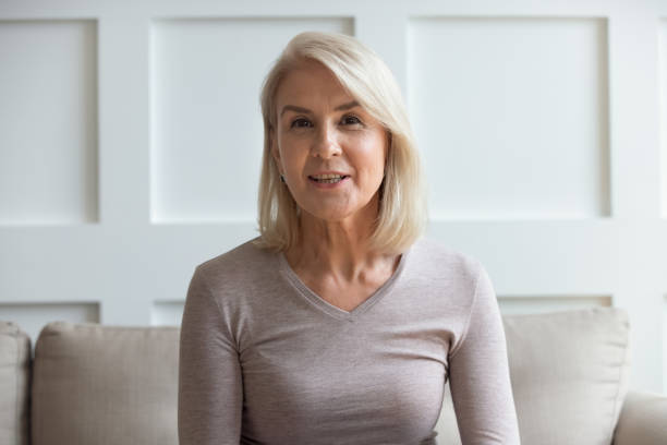 headshot portrait of mature woman sit on couch talking - looking in camera imagens e fotografias de stock