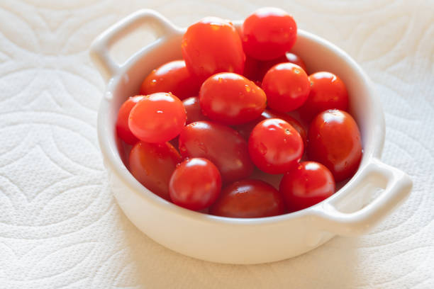 Close up of small bright fresh cherry tomatoes on a plate on white background