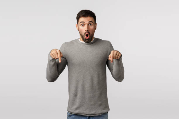 istock Surprised and speechless, excited handsome bearded guy feel emotional and impressed, folding lips in wow, amazement expression, pointing down, see stunning promo, want to try, show friends 1205454186