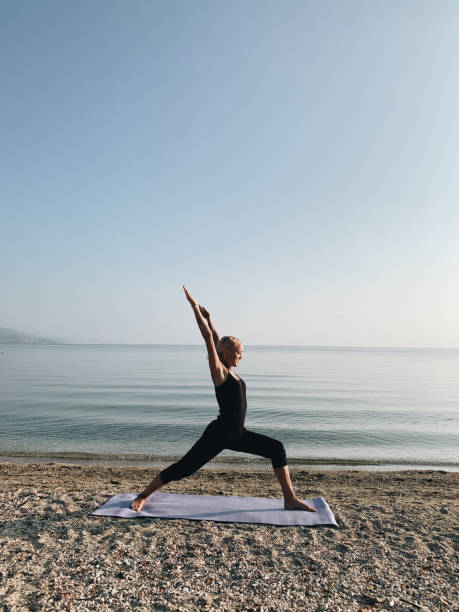 gadis pirang muda berlatih yoga prajurit asana di pantai laut saat matahari terbit - contributor potret stok, foto, & gambar bebas royalti