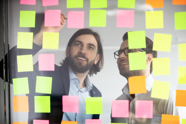 istock Two smiling businessmen writing tasks on sticky papers, post it 1205454426
