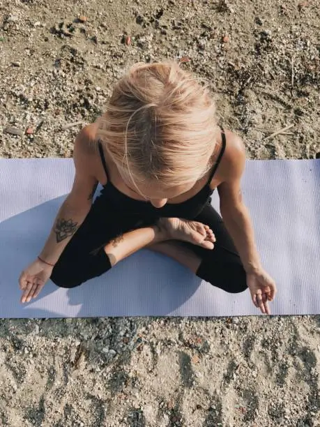 Top view of blond girl meditation in lotus pose on sea shore at sunrise.
