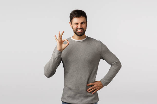 istock Everything under control. Sassy, assertive charismatic bearded man in grey sweater, wink confident, cant rely on me, show okay, ok gesture, approve product, like idea, accept plan, white background 1205455045