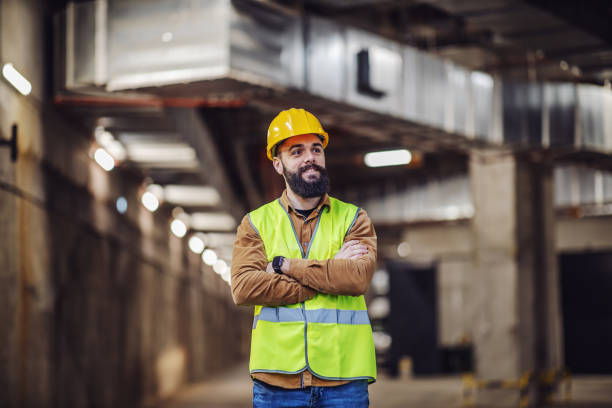 istock Young proud smiling attractive bearded supervisor standing in building in construction process with arms folded and overseeing his workers. 1205458190