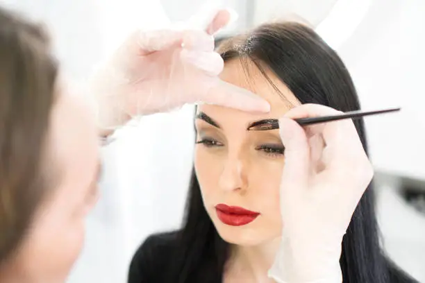 Makeup artist doing eyebrows tinting treatment for brunette woman.