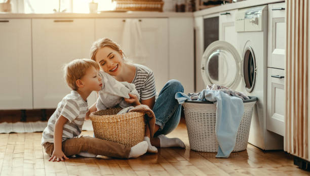 feliz familia madre ama de casa y el niño en la lavandería con lavadora - stereotypical housewife little girls family domestic kitchen fotografías e imágenes de stock