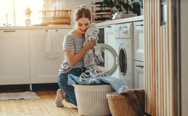 happy housewife woman in laundry room with washing machine - estereótipo de dona de casa imagens e fotografias de stock