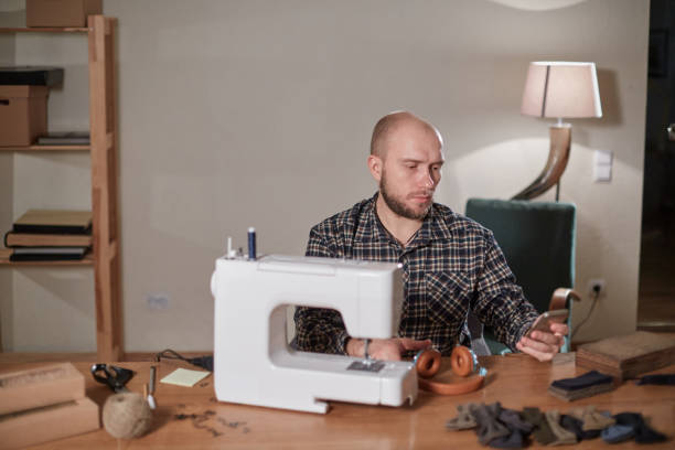 istock Man listen music and working with sewing machine in a textile studio. Tailor makes bow ties of woolen fabric. 1205462395