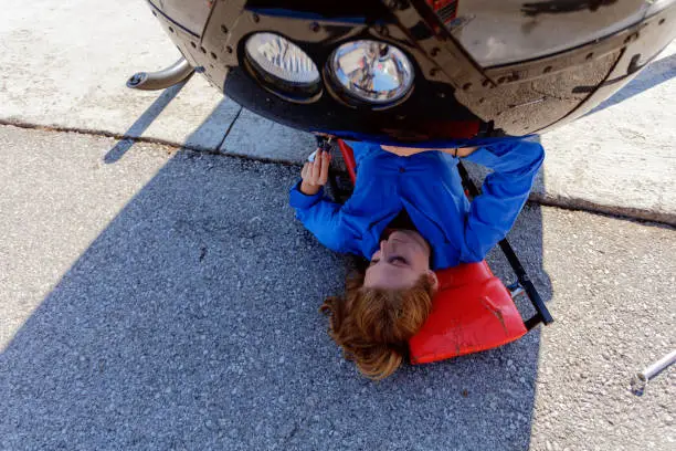 Young blonde woman lying on a cart under the helicopter cockpit and doing repairwork with screwdriver