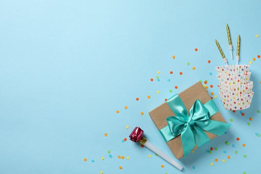 Gift box with bow and birthday accessories on blue background, top view