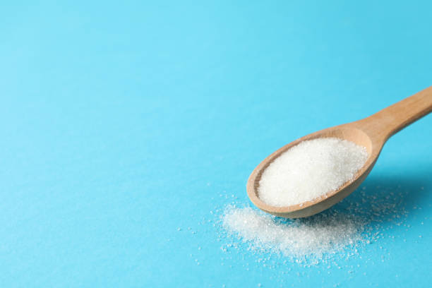 istock Spoon with sugar on blue background, close up 1205473199