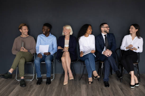 istock Six multiethnic employees sitting on chairs near black wall background 1205475188