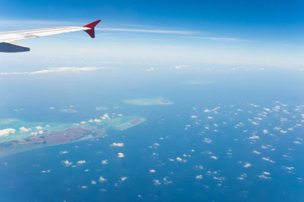 A small island on an open sea seen from a plane's window while flying over Indonesia. In the corner there is an air plane wing visible. Top down perspective.