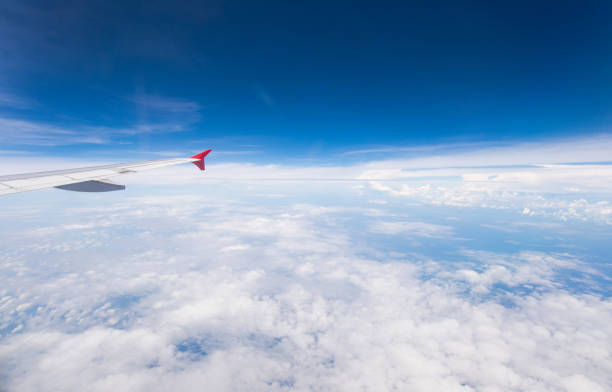 Wing of an airplane flying above the clouds with blue sky. View at the sky from the window of the plane.