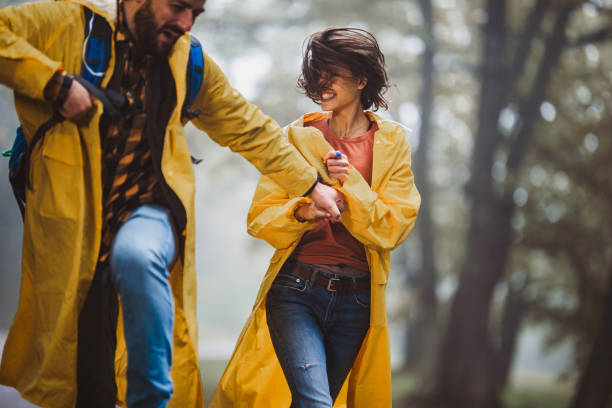 istock Playful couple in raincoats having fun while holding hands and running at the park. 1205476888