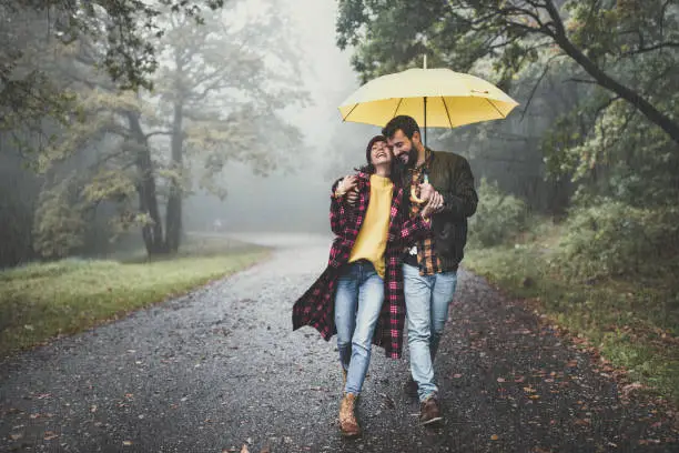 Cheerful embraced couple taking a walk on a rainy day at misty forest. Copy space.