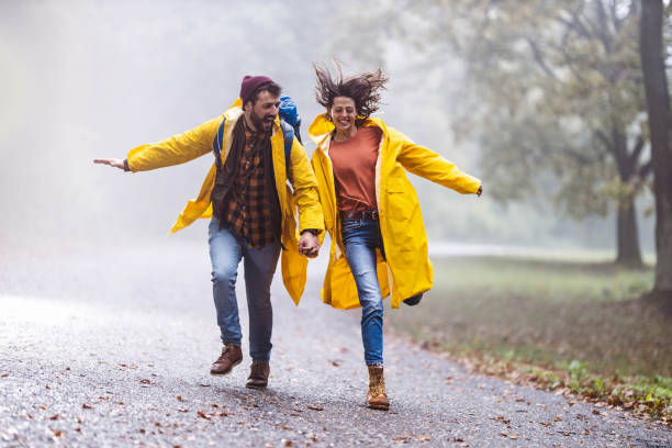 istock Cheerful couple in raincoats having fun during rainy day in forest. 1205477830