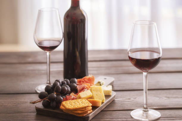 istock Red wine bottle with wine glasses and cheeseboard with cheese, ham, grapes and crackers on brown wooden table. Food and wine concept. 1205479127
