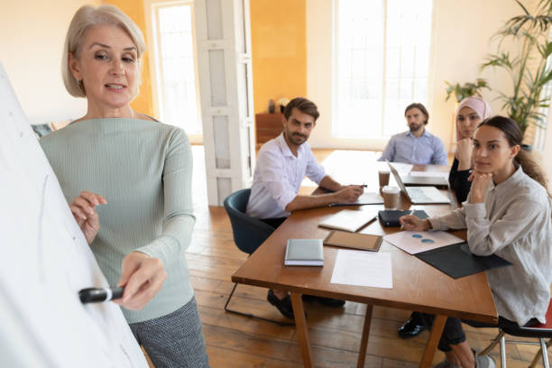 istock Mature female speaker make whiteboard presentation to employees 1205480361