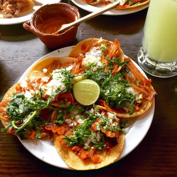 A plate of delicious tacos al pastor, seasoned and grilled pork meat with onions and coriander toppings, with hot sauce and lemonade. Gourmet twist on traditional mexican street food in Mexico City.