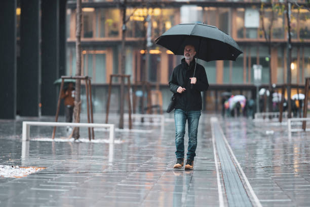 istock man with umbrella walking through rain in city 1205485342