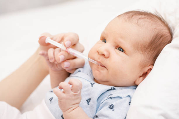 Mother feeding newborn baby with liquid Vitamin K Mother feeding newborn baby with Vitamin K using plastic syringe to prevent Vitamin K deficiency bleeding (VKDB) known as Haemorrhagic disease of the newborn babyhood photos stock pictures, royalty-free photos & images