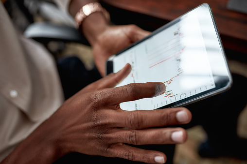 Close up shot of hands holding tablet pc. Trader is using touch screen tablet for analyzing stock market chart, while working in the office. Trading, business concept.