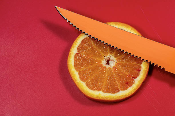 Close-up of a fresh slice of an orange on a red cutting board with an orange knife