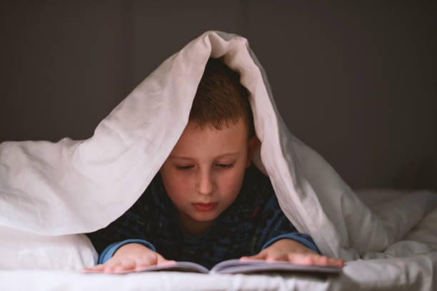 istock Little boy reading book in bed 1205486741
