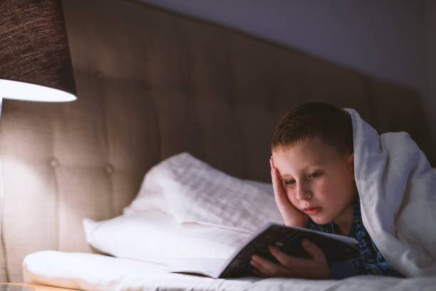 istock Little boy reading book in bed 1205488965