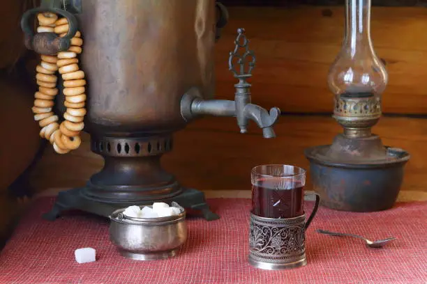 On the table is a glass of black tea by an old samovar and a lamp.