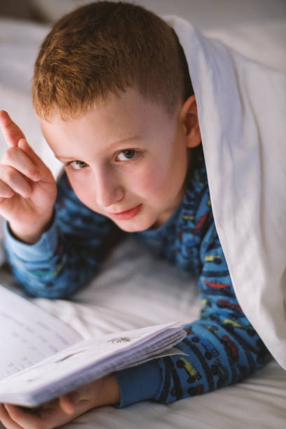 istock Little boy reading book in bed 1205490743
