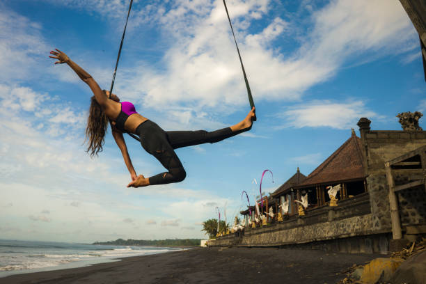 aero yoga beach workout - young attractive and athletic woman practicing aerial yoga exercise training acrobatic body postures on blue sky over sea in Bali island healthy lifestyle concept entrenamiento de playa de yoga aero - joven atractiva y atlética mujer que practica ejercicio de yoga aéreo entrenamiento de posturas del cuerpo acrobático en el cielo azul sobre el mar en la isla de bali concepto de estilo de vida saludable