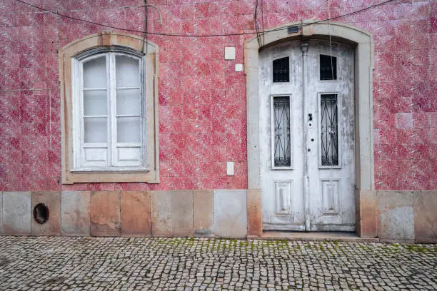 Lovely white door surrounded by pink tiles in Silves, Portugal, with cobblestone street