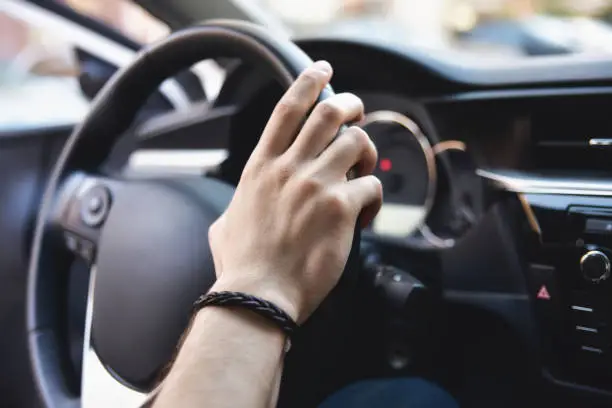 Photo of Male arms holding leathern rudder of car