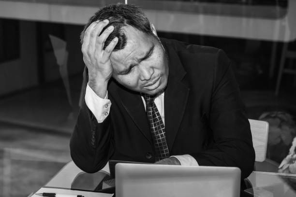 An Asian male businessman is sad and crying in front of the computer laptop for his failure management in finance business investigation work and job during a strong economic crisis issue stock photo