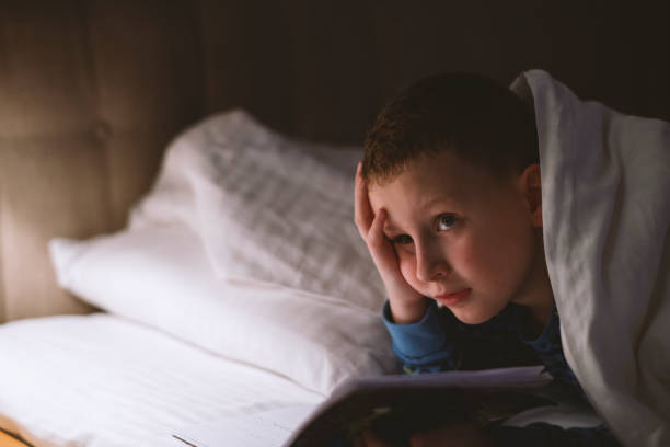 istock Little boy reading book in bed 1205492972