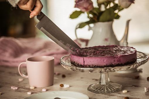 Close up of a vegan purple raw cake being cut by a female hand with a knife.
